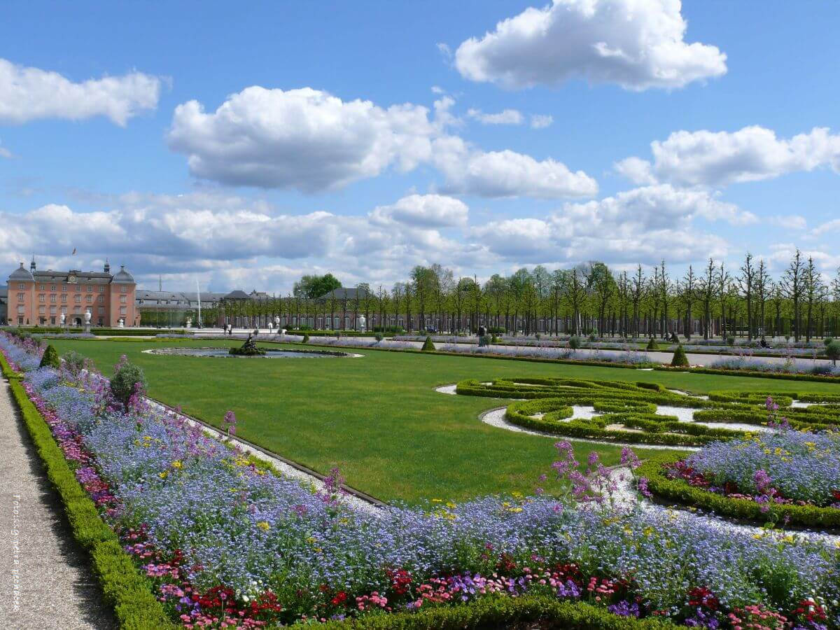 Blick über den Schwetzinger Schlossgarten mit gepflegten Wegen, grünen Hecken und historischen Bauwerken. 