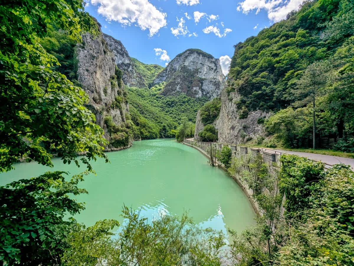 Panoramablick in die tiefe Furlo-Schlucht in den Marken, mit einem türkisen Fluss, einer Straße und üppig grünen, steilen Felswänden unter blauem Himmel.