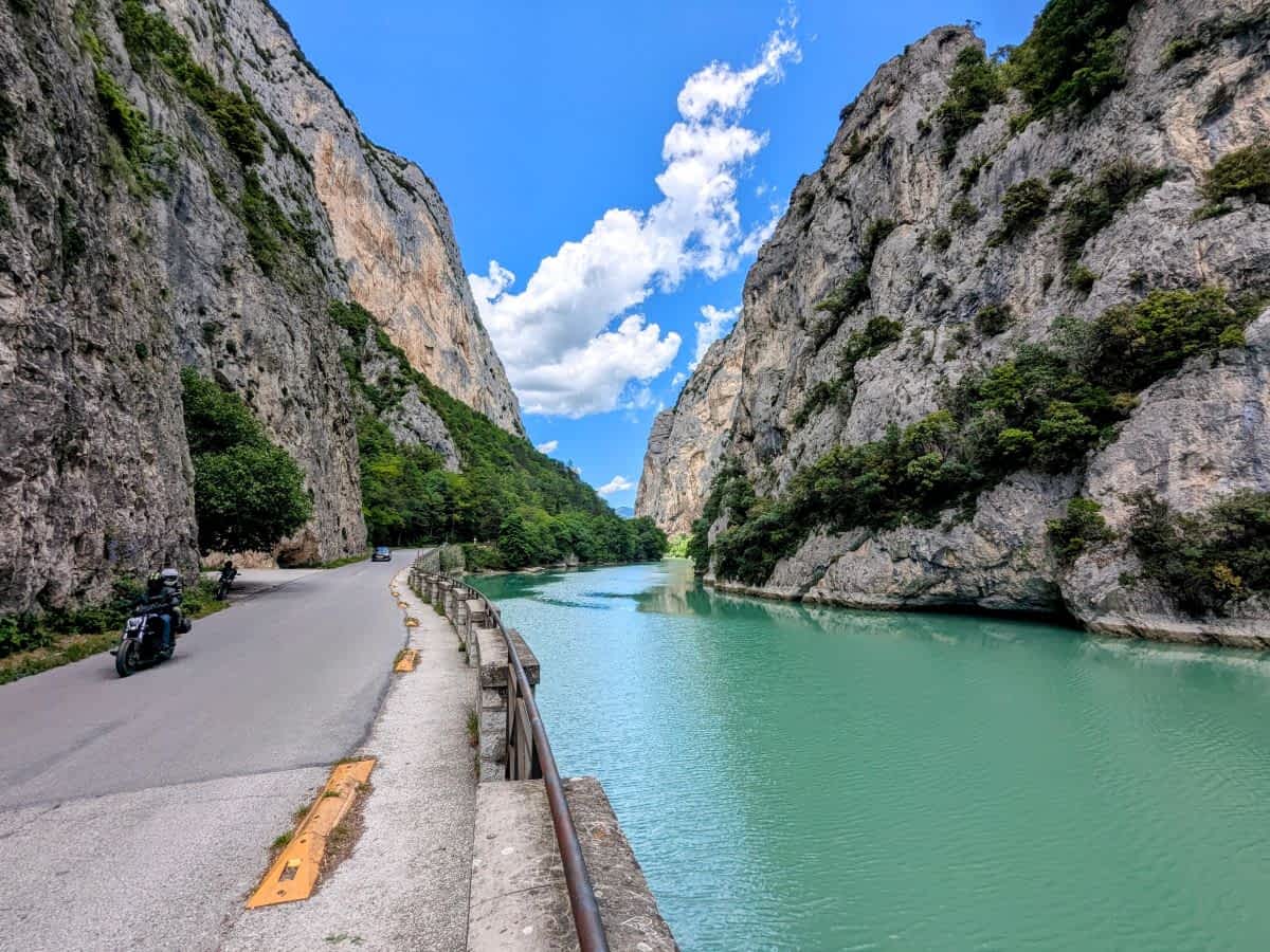 Die Straße schlängelt sich hier direkt am leuchtend grünen Fluss entlang, eingerahmt von imposanten, teils überhängenden Felswänden – ein Paradies für Naturliebhaber und Motorradfahrer.
