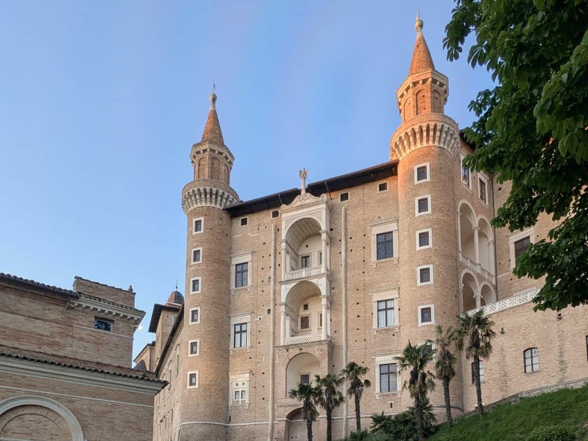 Detailansicht der markanten Türme und Fassade des Herzogspalastes von Urbino bei blauem Himmel.