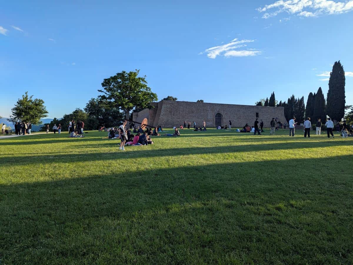 Große grüne Wiese des Parco della Resistenza in Urbino mit Menschen, die sich entspannen und einer Festung im Hintergrund