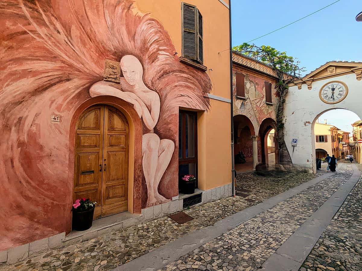 Eines der bekanntesten Wandgemälde von Dozza, die eine elfenhafte Figur zeigt. Im Hintergrund sehen Sie das Tor zur Altstadt.