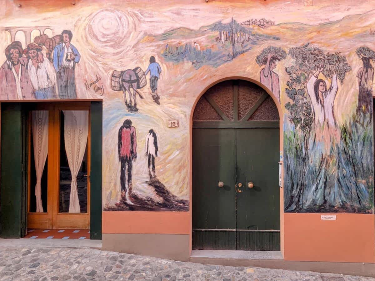 Fassade in Dozza, Italien, mit einem farbenfrohen Wandgemälde, das Bauern und eine weibliche Figur mit Weinreben darstellt.