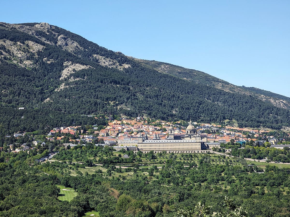  Blick von einem Hügel auf das Kloster El Escorial, umgeben von Wäldern und Bergen