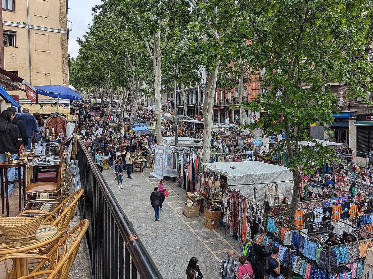 Straße voller Marktstände mit Kleidung, Antiquitäten und Besuchern beim Stöbern.