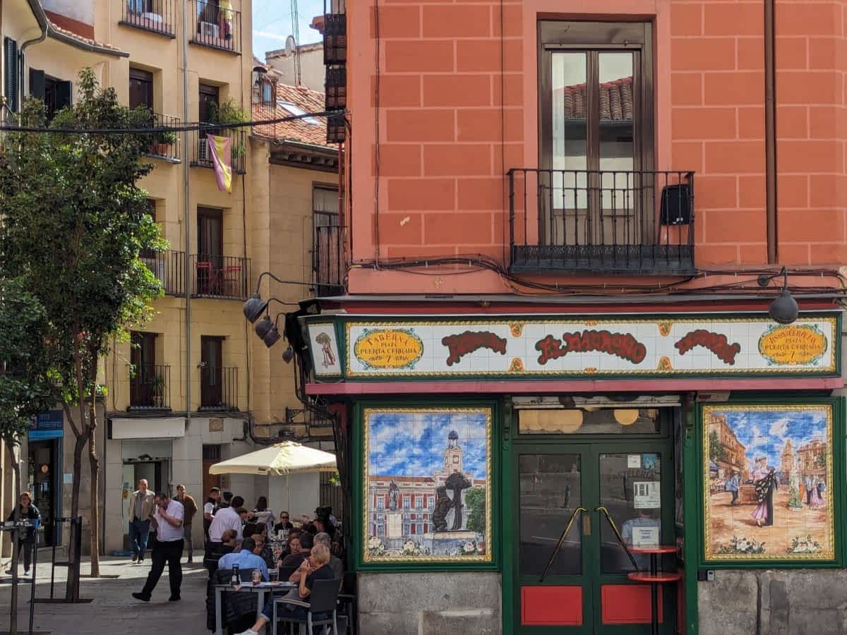 Schmale, belebte Straße mit bunten Häusern, Cafés und Menschen im Viertel La Latina.