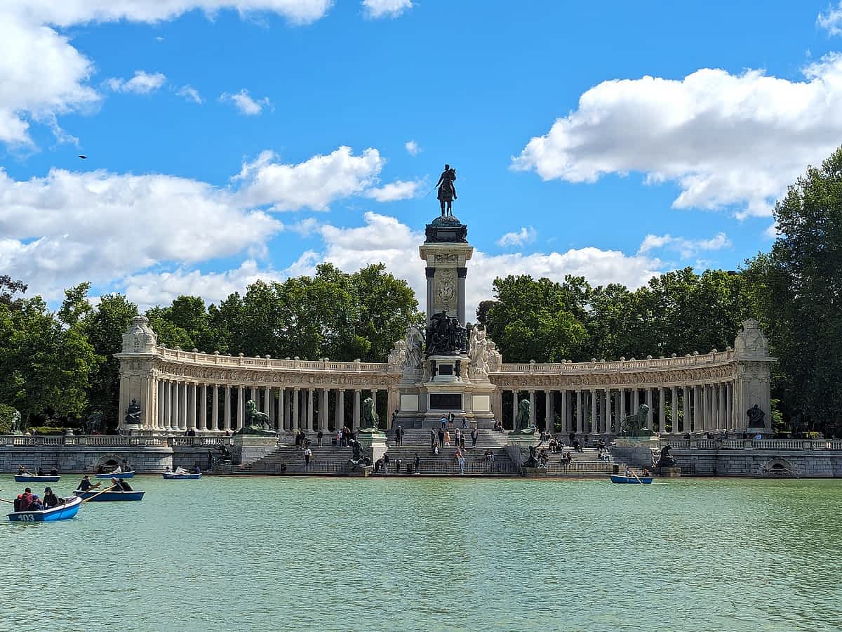 Menschen in blauen Ruderbooten auf dem See im Retiro-Park vor dem Monument.
