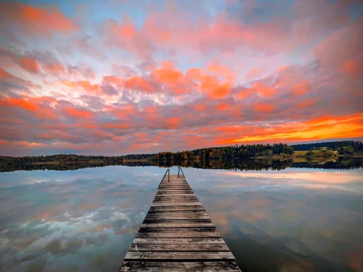 Traumhafter Blick über den  Pelhamer See mit  Holzsteg. Der orange-rot gefärbten Himmel spiegelt sich im See.